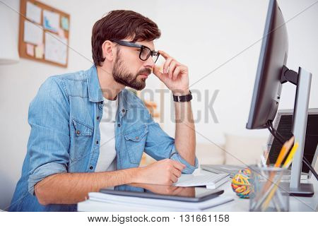 Concentrated on work. Serious young man thinking over and touching his glasses while looking at the screen of his computer