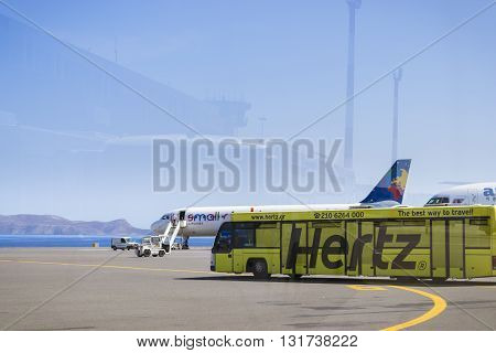 HERAKLION GREECE - APRIL 28 2016: Aircraft Airbus A320 Polish airlines Small Planet is on pre-flight preparation at Heraklion Airport N. Kazantzakis. In foreground is yellow bus Cobus 3000. In reflection on glass is visible the profile of airport building