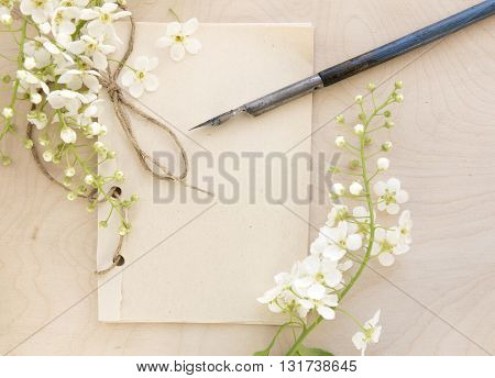 Open vintage handmade sketchbook with white bird-cherry flowers over wooden table background. Mock up retro style. Old paper notepad. Vintage retro mockup. Rough rope. Summer mock-up. Wooden background. Old pen.
