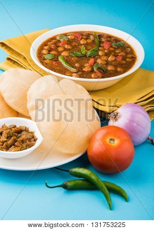 spicy chick peas also known as Chola Masala or Chana Masala or Chole served with fried puri, pickle and green salad