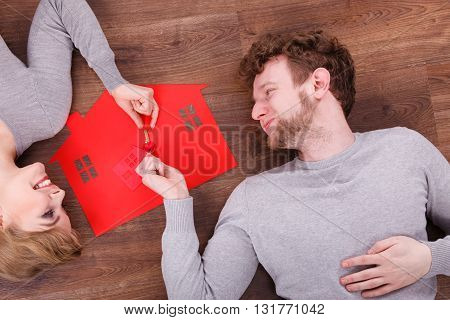 Home security safety future family mortgage finances concept. Young couple exchanging keys. Man and wona lying on floor with house cutout.