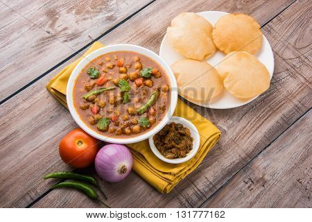 spicy chick peas also known as Chola Masala or Chana Masala or Chole served with fried puri, pickle and green salad