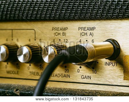 Macro photo of a vintage electric guitar amplifier showing the knobs and input plug.