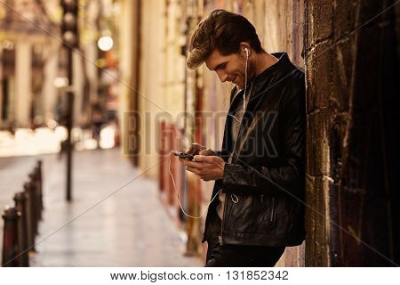 Young man listening music with smartphone earphones in the street