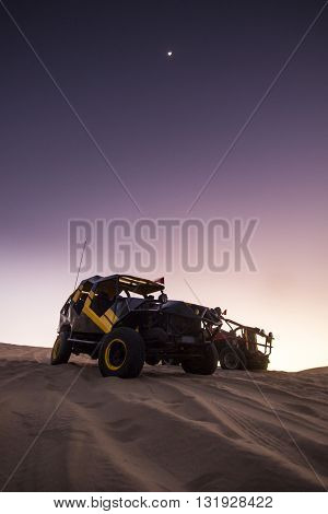buggy on sand dunes at purple sunset in huacachina, peru