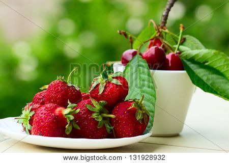 Group of fresh spring fruits together cherries and strawberries. Cherries in white bowl.Strawberry on a wooden background. Red strawberries. Strawberries on green
