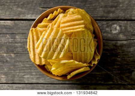 Crinkle cut potato chips on kitchen table. Tasty spicy potato chips in bowl. Top view.
