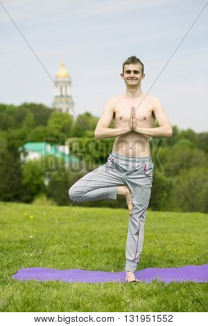 Young Adult Doing the Tadasana Tree position in Yoga on a Stump in Nature. Man doing yoga exercises in the park
