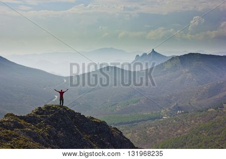 man standing on a cliff in mountains with snowy picks and blue sky with clouds on background