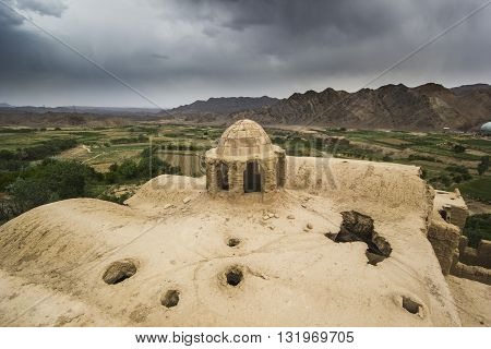 roofs of abandoned city Kharanak, Iran, yazd and gardens near city with massive clouds on sky