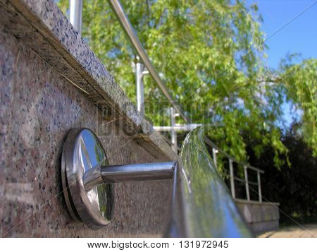 Trees and sky reflected in a steel handrail marble stairs in the park