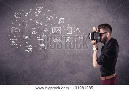 An elegant hipster guy trying to use a vintage camera with camera settings icons drawn on wall, like flash, white balace or ISO value concept