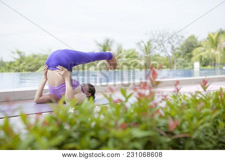 Woman Playing Yoga Beside Swimming Water Pool With Beautiful Natural Green Leaves