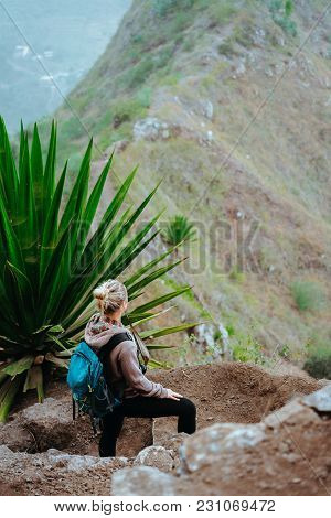 Woman With Backpack On The Trekking Route Near Mountain Edge Looking Down To Valley. Santo Antao Isl