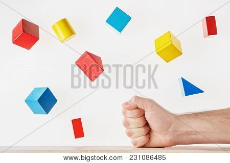 The Fist Strikes The Table And The Multicolored Wooden Geometric Shapes Fly Around. Concept Of Creat