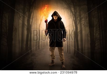 Mysterious man coming from a path in the forest with burning flambeau concept