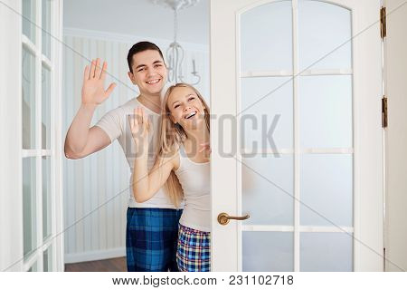 A Happy Couple In Their Pajamas Opens The Door Invites To Their House.