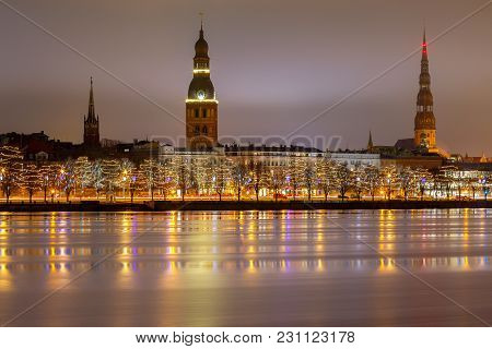 Central Embankment Of The Daugava River And The Spiers Of The Churches At Night.