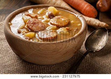 Wooden Bowl Of Split Pea Soup With Sausage And Potatoes
