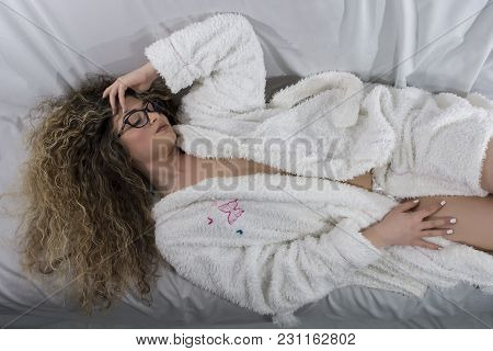 Woman With Curly Hair Dressed In Fluffy Robe Posing Sexy On Bed