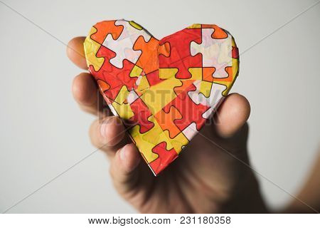 clousep of a young caucasian man holding a heart patterned with many puzzle pieces of different colors, symbol of the autism awareness