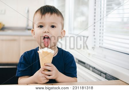 A Child In A Dark-blue T-shirt In The Bright Kitchen Eating A Waffle Ice Cream Cone In The Summer Ho