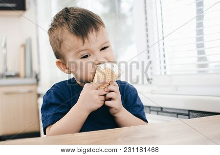 A Child In A Dark-blue T-shirt In The Bright Kitchen Eating A Waffle Ice Cream Cone In The Summer Ho
