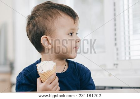 A Child In A Dark-blue T-shirt In The Bright Kitchen Eating A Waffle Ice Cream Cone In The Summer Ho