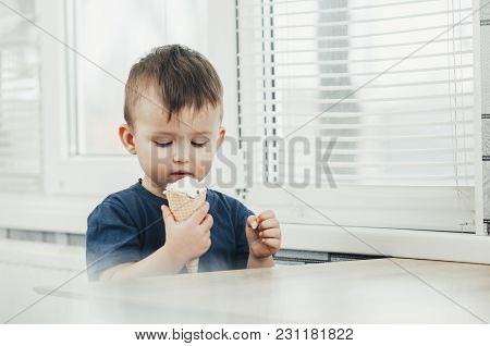 A Child In A Dark-blue T-shirt In The Bright Kitchen Eating A Waffle Ice Cream Cone In The Summer Ho