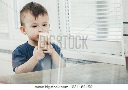 A Child In A Dark-blue T-shirt In The Bright Kitchen Eating A Waffle Ice Cream Cone In The Summer Ho