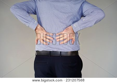 Close-up View Of A Young Man With Pain In Kidneys On Gray Background. Businessman With Back Ache Cla