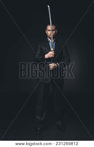 Man In Suit Holding Japanese Katana Sword In Front Of His Face On Black