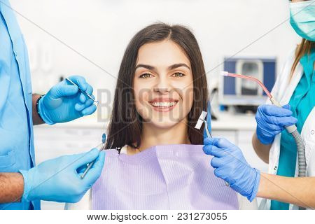 Smiling Beautiful Patient Sitting In Chair With Dental Purple Bib, Male Dentist, In Blue Uniform And