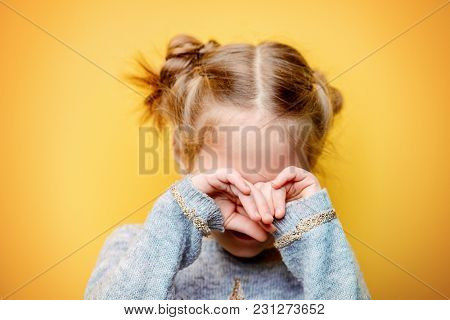Close-up portrait of an offended crying little girl. Yellow background. Childhood concept.