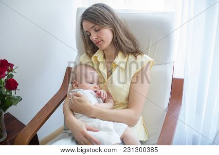 Young Mother Holding Her Baby, Rocking Him To Sleep, Sitting In Armchair