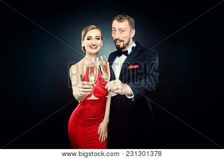 Elegant woman and man clinking glasses on glamourous party wearing formal dinner jacket and evening dress