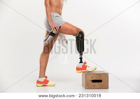 Half portrait of a young disabled sportswoman with leg prosthesis standing with water bottle isolated over white background