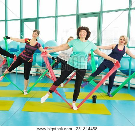 50-year Woman Doing Exercise With Latex Fitness Band During Workout In A Gym.