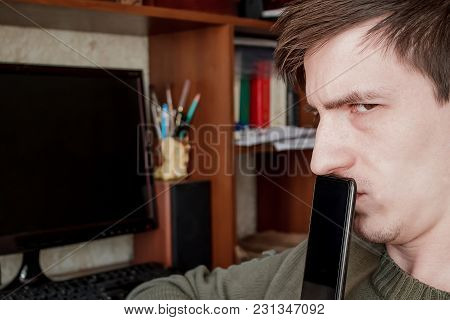 The Guy Suspiciously Looks Into The Camera, Closed The Rum With A Black Smartphone, In The Workplace