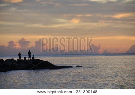Peole Are Fishing On The Rocks Near The Ocean  At Sunset