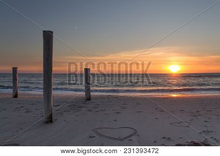 Beautiful Sunset At The Beach With Wooden Piles And Hearts Drawings In The Sand Petten, Holland, Nor