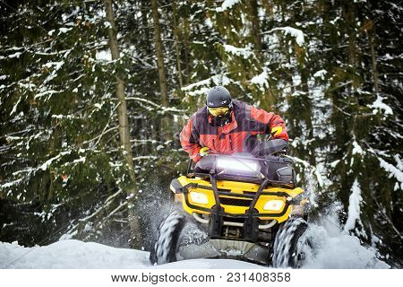 A Man Is Riding An Atv In Winter On The Snow In His Helmet.