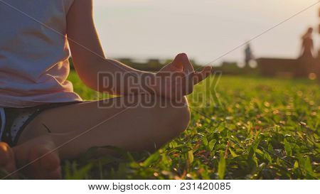 Little Cute Girl Meditates In Turkish Pose In The Park At Sunset. Crop Part Body And Hand With Youga
