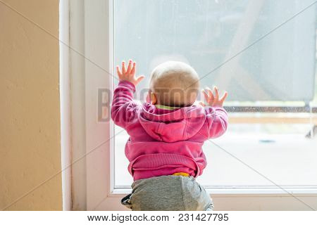 Baby Girl Looking Through Balcony. Leaning On Glass And Exploring.