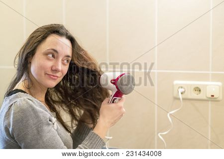 Young Woman With Brown Hair Drying Hair With Electric Blowdryer At Home.