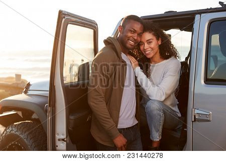 Young mixed race couple on a road trip embracing by car