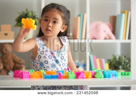 Little Girl Playing With Plastick Blocks At Table In Nursery Room