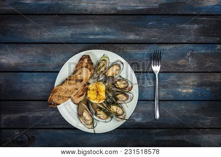 Mussels And Bread Toasts On On A White Plate. Served With Half Grilled Lemon And Fork. Dark Blue Woo