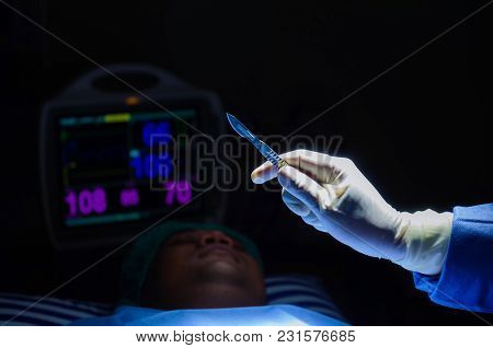 Doctor's Hand Holding A Scalpel Knife Surgeon Work While Patient On Bed With Ecg/ekg Monitor Showing
