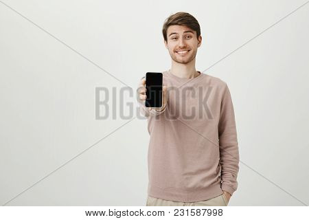 Studio Portrait Of Happy Attractive European Male Model Showing Smartphone At Camera While Smiling A